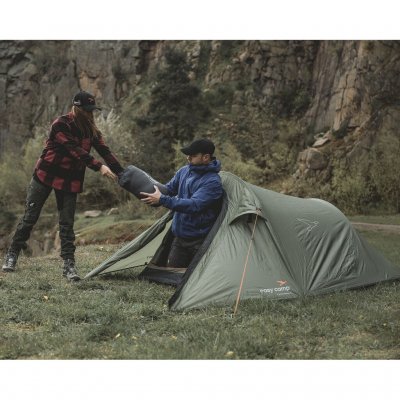 Reindal 2 tunneltelt i naturmiljø, to personer bærer sovepose gjennom teltets åpne inngang.